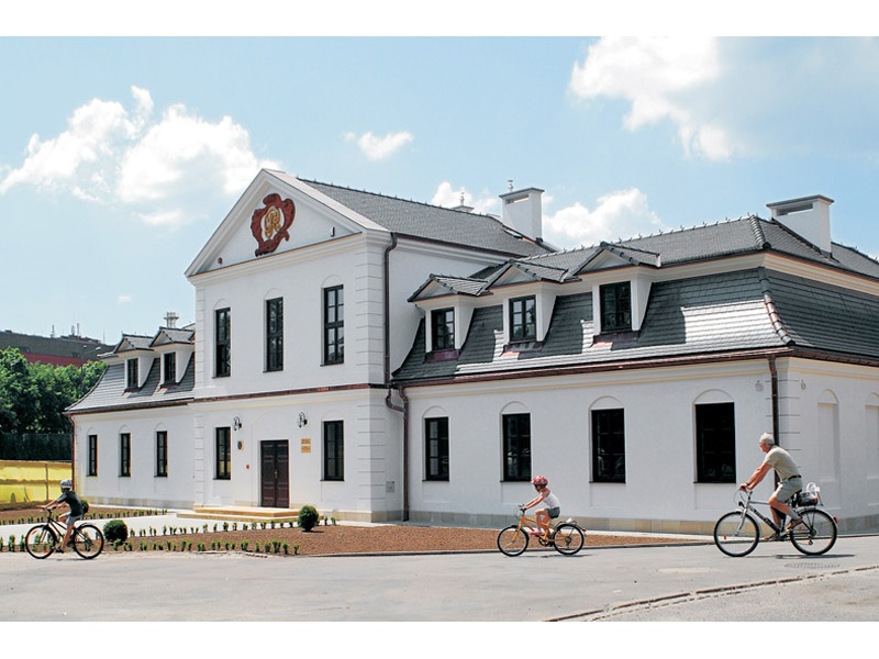Zdjęcie przedstawia odrestaurowany budynek dworkowy z rowerzystami na pierwszym planie.