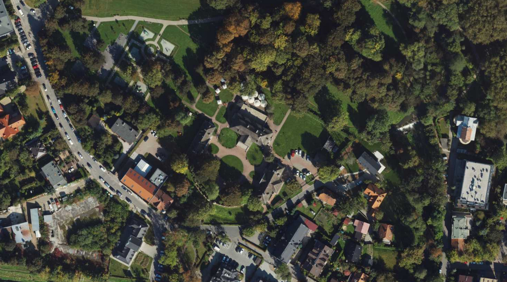 Zdjęcie przedstawia widok z lotu ptaka na zielony park otoczony zabudową mieszkalną.